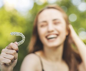 Smiling woman outside holding Invisalign in Cleburne, TX
