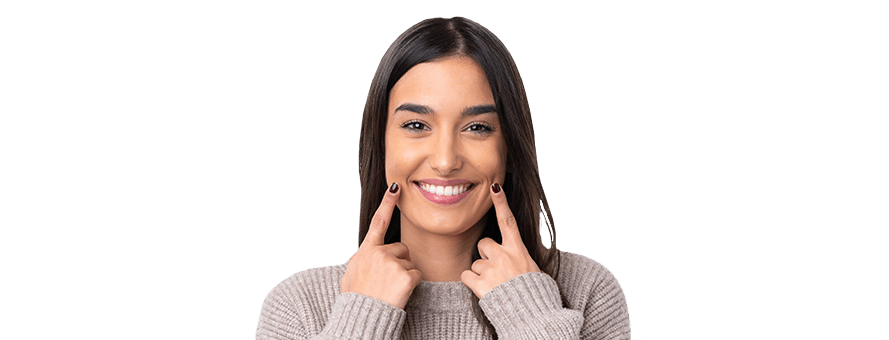 A young woman wearing a yellow sweater and pointing to her smile after seeing her orthodontist in Cleburne