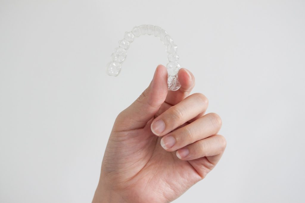 Patient holding up clear aligner against grey background