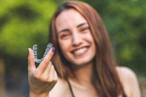 Woman smiling while holding up Invisalign tray